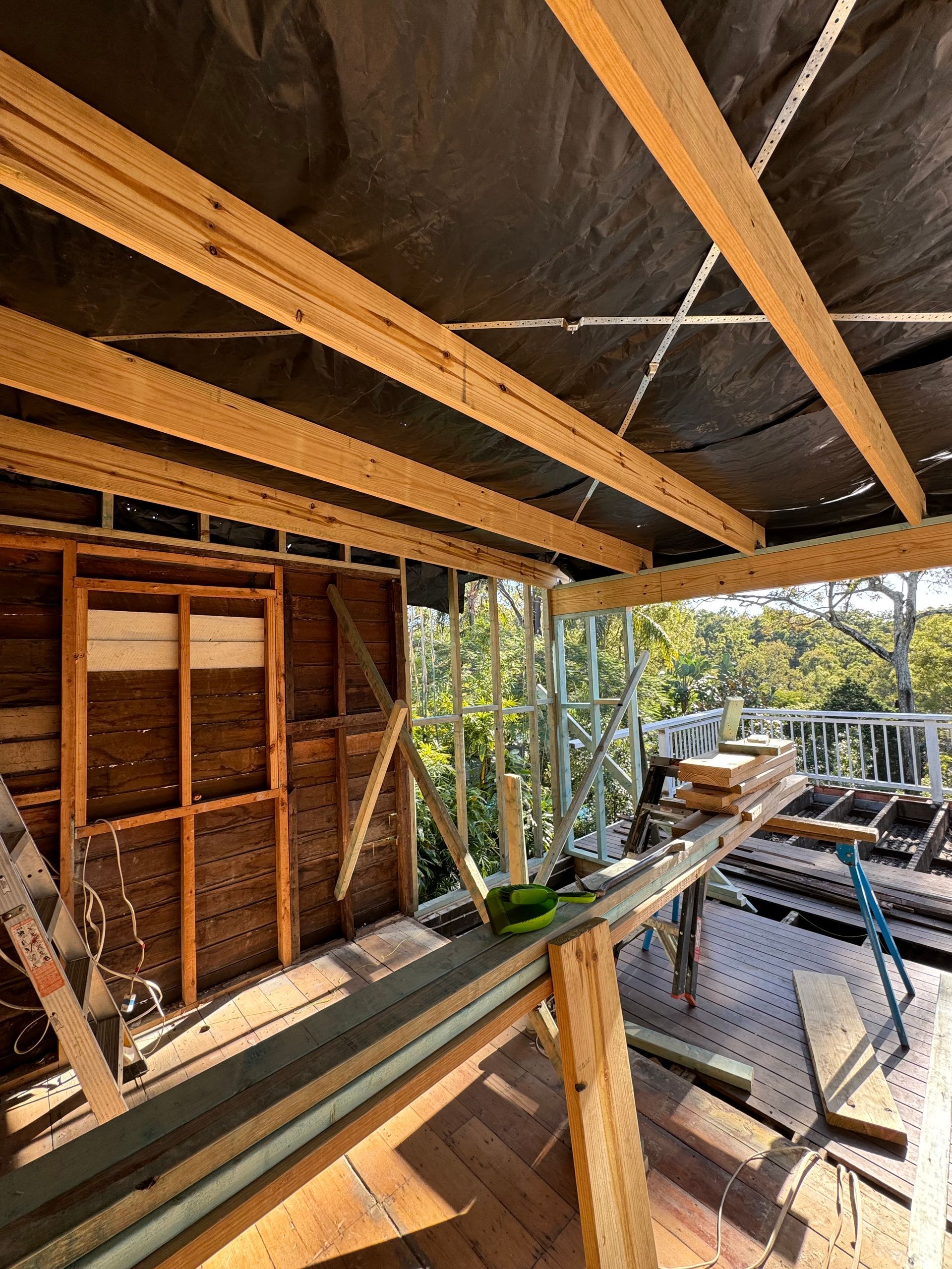 Construction site: wooden beams forming a roof structure. A half-built deck with views of trees.